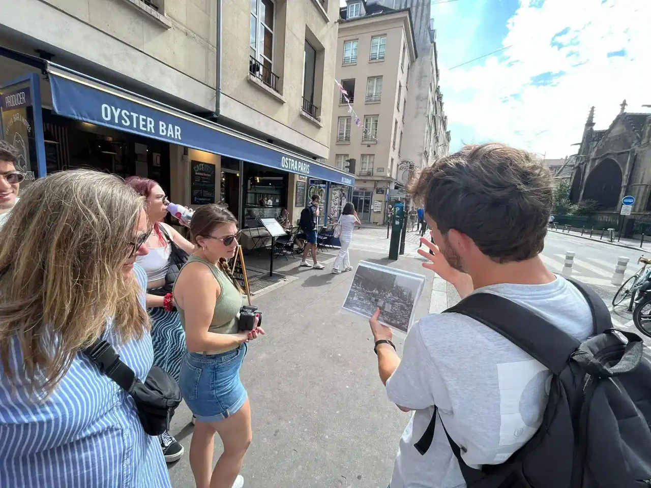 Clément showing a tour group an archive photograph of a 1944 barricade, in the street near the church of Saint-Séverin