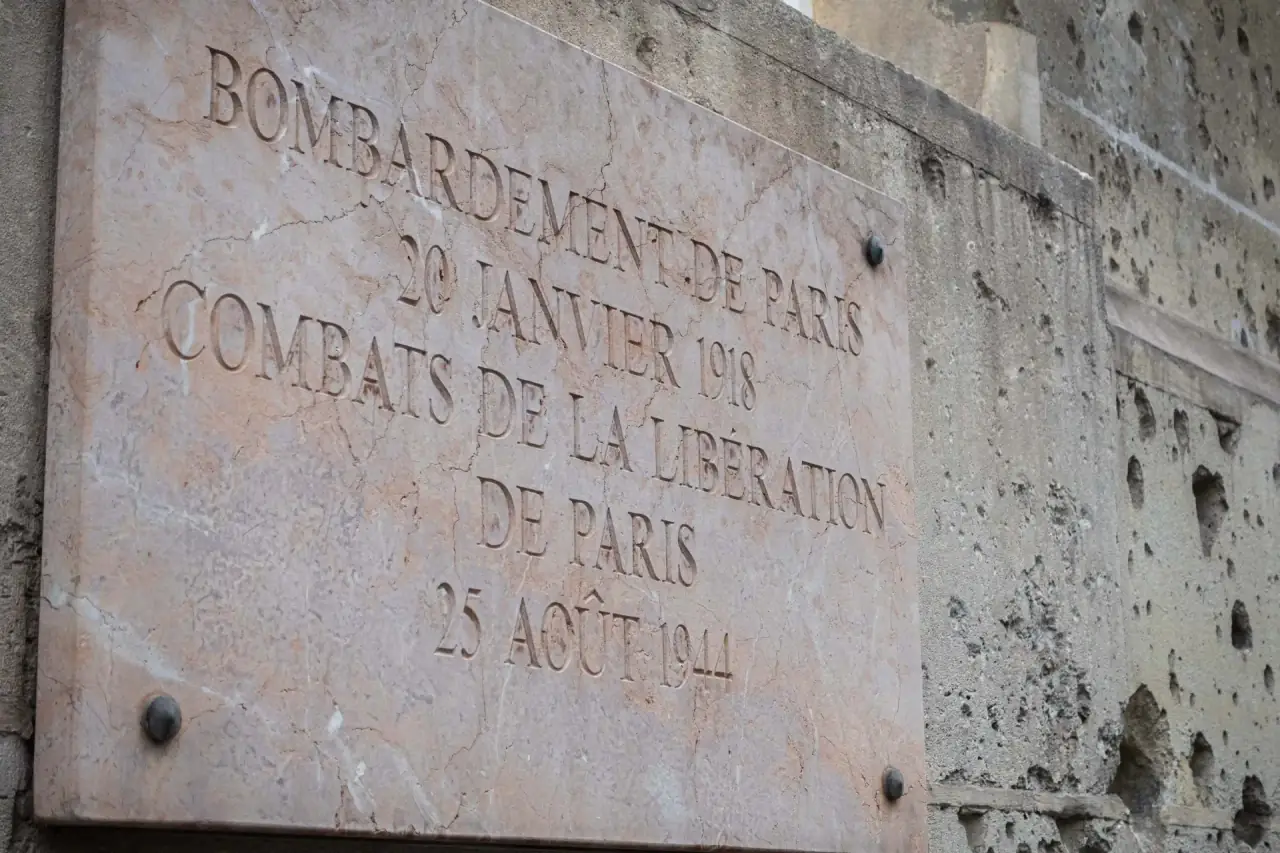 Marble plaque on the École des Mines reading 'Bombardement de Paris 20 janvier 1918 — Combats de la Libération de Paris 25 août 1944', beside a wall pitted with bullet impacts